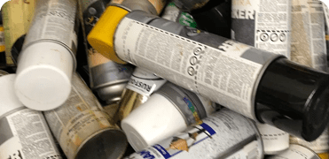 Many cans of paint are piled up on top of each other.