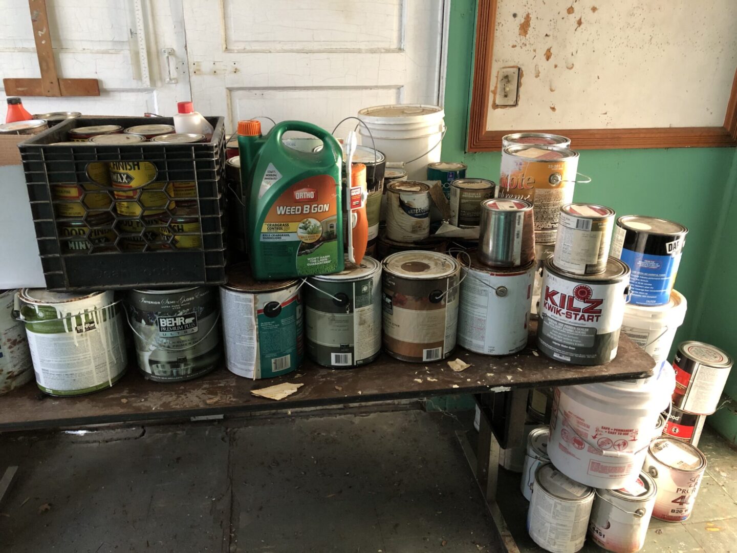 Many cans of paint sit on a table in a room.