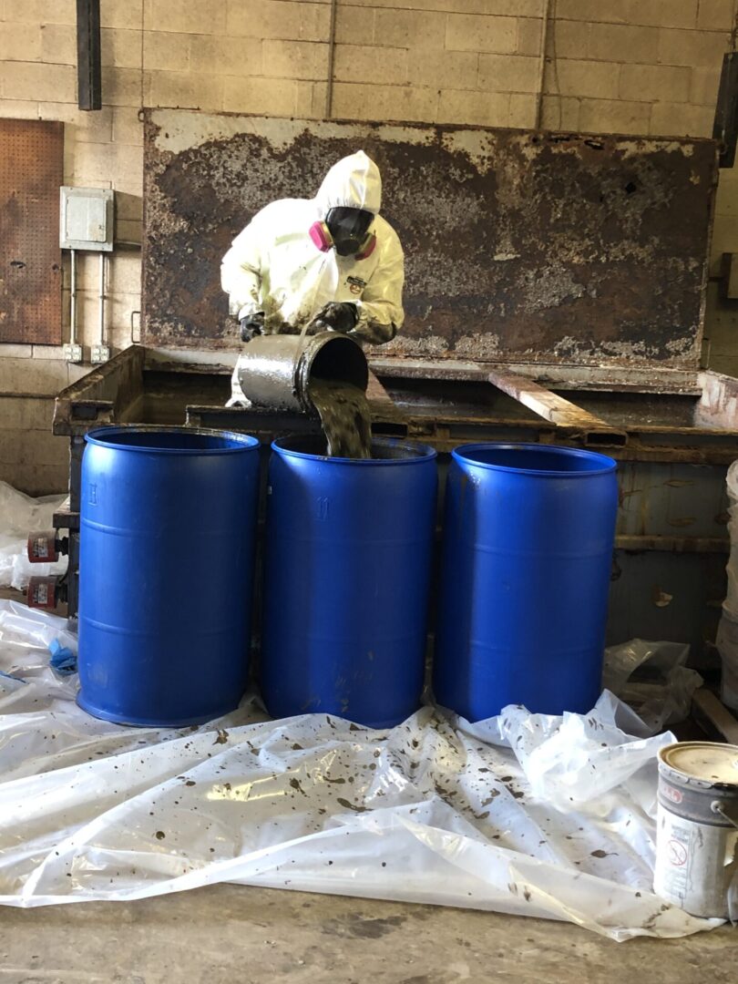 A man in a protective suit working with blue barrels.