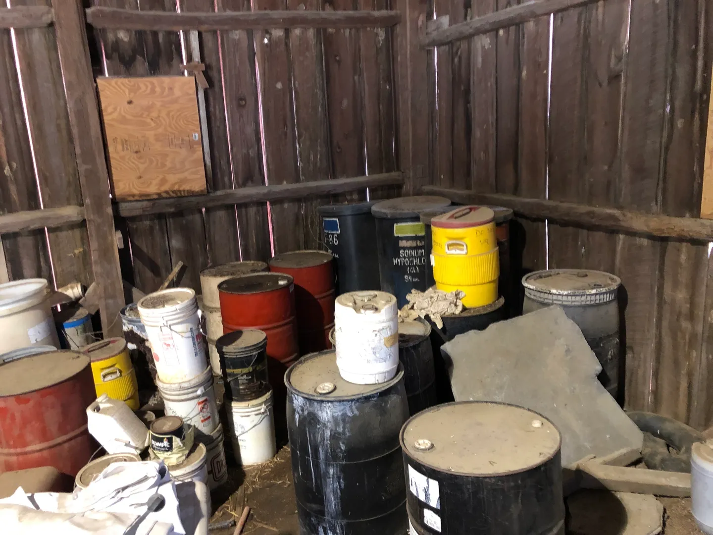 Various chemical barrels and containers in a barn.