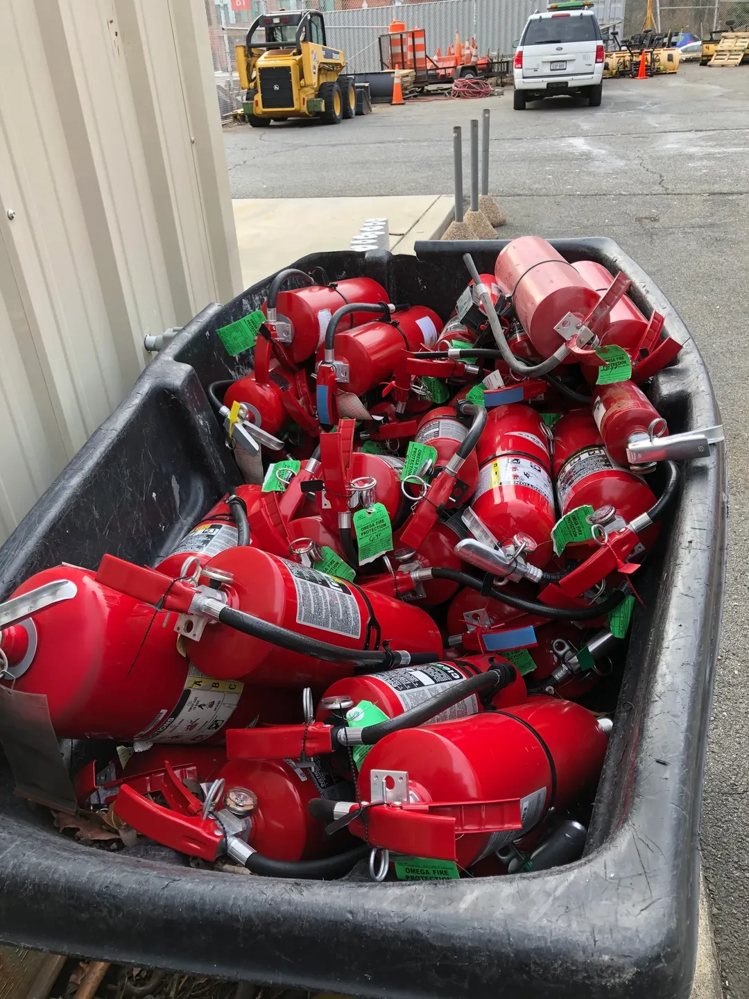 A large black bin full of red fire extinguishers.